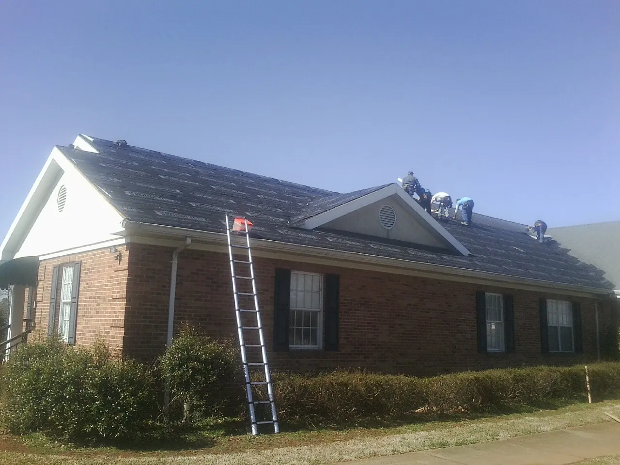 Crew tearing shingles off a brick ranch roof with a ladder set — Emergency Roof Repair work by our crew in Reesville