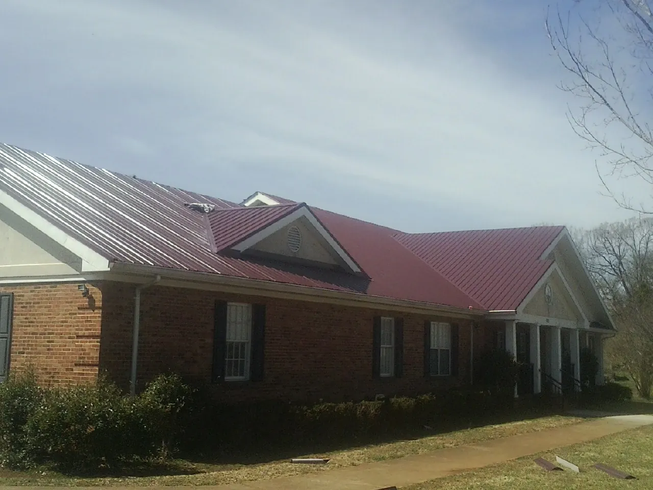 Red metal roof with gabled entries on a long brick building, from a Hail Damage Roof Repair job in Reesville