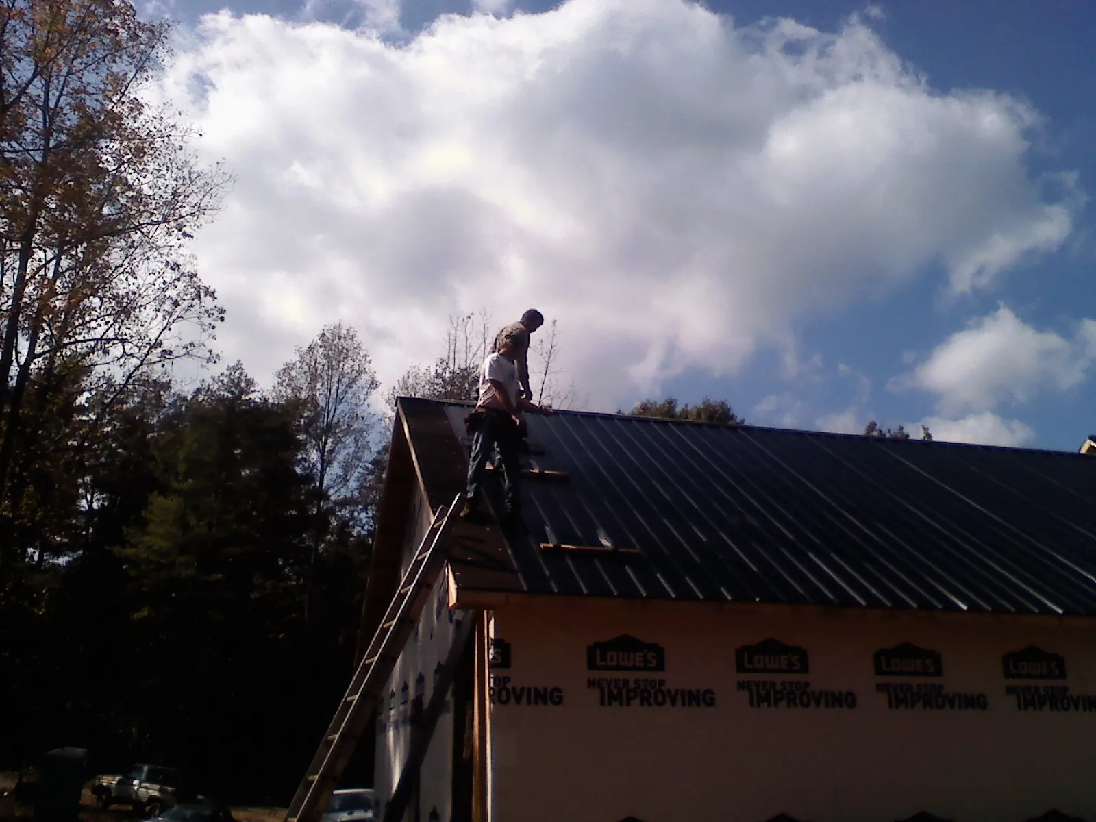 Roofer fastening dark metal panels high against a cloudy sky, from a Roof Inspection job in Reesville